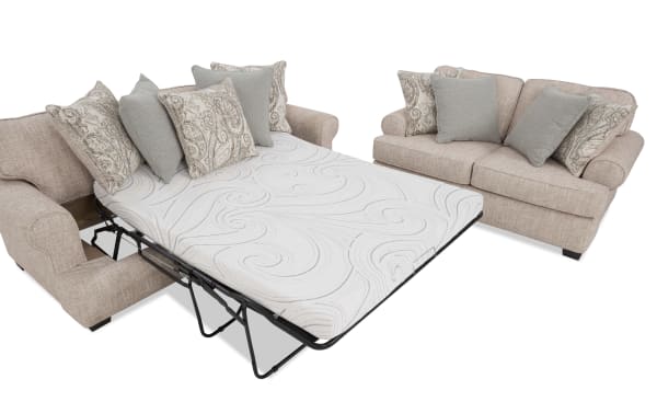 Beige fabric sectional sofa with a pull-out queen-size mattress bed featuring a white patterned mattress and multiple decorative throw pillows in neutral tones.
