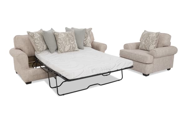 Beige fabric sofa set with a queen-size pull-out bed mattress, featuring rolled arms and decorative patterned and solid throw pillows.