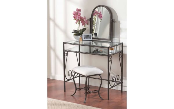 Levi Bronze Vanity Set with beige polyester cushioned stool, transitional style steel frame with swirly design, glass top and shelf, and arched mirror.