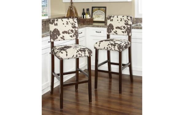 Corey Udder Madness bar height stool with brown and white cow print polyester fabric, antique bronze nailhead trim, and Manhattan stain rubberwood legs.