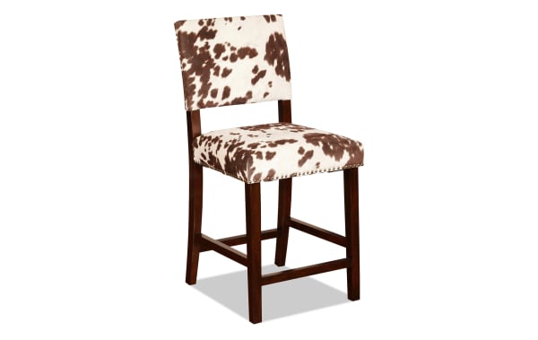 Corey Udder Madness multi upholstered counter height stool with brown and white cow print polyester fabric, antique bronze nailhead trim, and Manhattan stain rubberwood legs in transitional style.