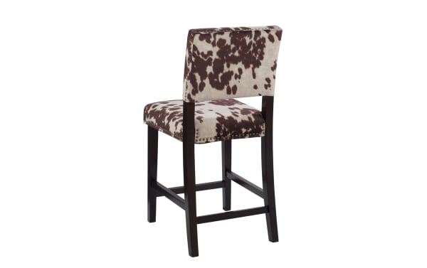 Corey Udder Madness multi upholstered counter height stool with brown and white cow print polyester fabric, antique bronze nailhead trim, and Manhattan-stained rubberwood legs.