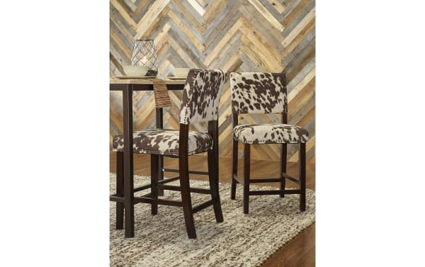 Corey Udder Madness multi upholstered counter height stool with brown and white cow print polyester fabric, antique bronze nailhead trim, and Manhattan stain rubberwood legs.