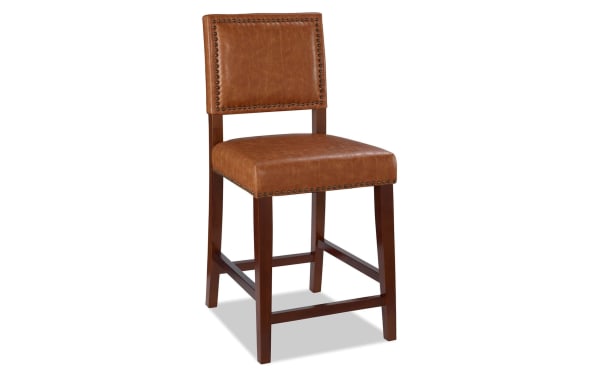Marie Camel faux leather upholstered counter height stool with nailhead trim, rubberwood frame, and contemporary brown polyurethane seat and back.