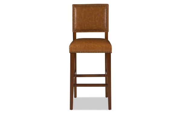 Marie Brown faux leather upholstered bar height stool in camel with nailhead trim, rubberwood frame, and contemporary style for kitchen or counter seating.