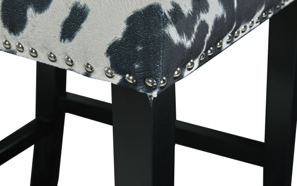 Corey Black & White Upholstered Bar Height Stool with cowprint polyester fabric, matte black rubberwood legs, and silver nailhead trim, traditional style.
