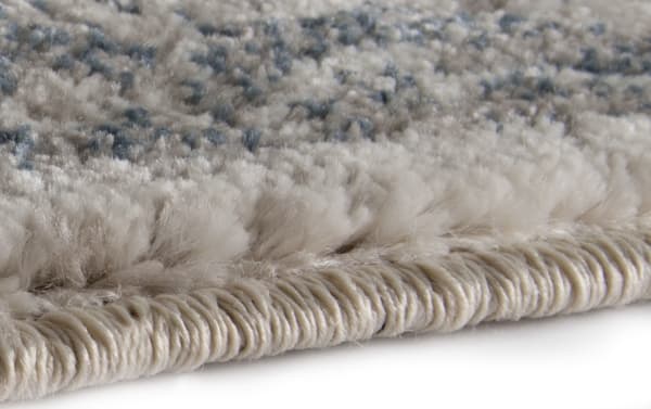 Close-up of the Lilah 5' x 7' Blue Damask Rug edge showing soft, dense polypropylene fibers in blue and cream with a tightly woven border, highlighting its transitional style and durable polyester-polypropylene fabric blend.