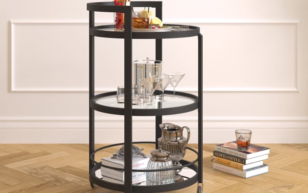 Contemporary Constance Blackened Bronze Bar Cart with steel frame, tempered glass shelves, mirrored bottom, sturdy railings, and casters for mobility.