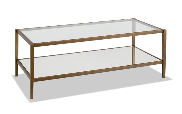 Patricia Brass Coffee Table with glam brass-finished steel frame, tempered glass top, and mirrored lower shelf for elegant living room storage.