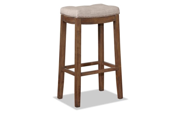 Ryann Gray Upholstered Backless Bar Height Stool with gray linen fabric seat, rustic rubberwood frame, and silver nailhead trim in transitional style.