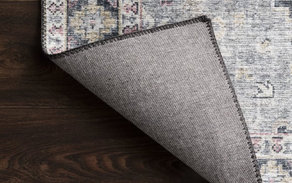 Corner view of the Lyudmila 8' x 10' Charcoal Oriental Rug showing its traditional multicolored old-world design with charcoal, gray, blush, and gold tones, crafted from durable 100% polyester fabric with a tightly woven texture and stitched edges, ideal for adding timeless style and high-end look to any room.
