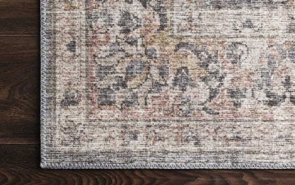 Corner close-up of the Candis 8' x 10' Gray Oriental Rug showing a traditional multicolored pattern in gray, blush, ivory, and charcoal on polyester fabric with a stitched edge.