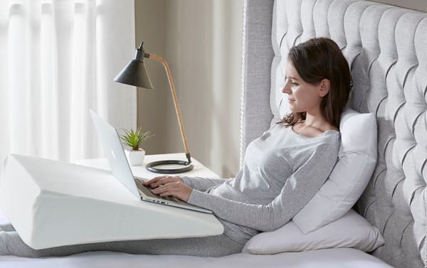 Person using a white transitional style Memory Foam Wedge Pillow with a washable soft knit cover, supporting legs while working on a laptop in bed.