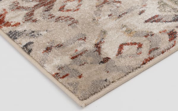 Corner close-up of the Solis 3' x 5' Beige Ikat Rug showing its cream base with red, blue, orange, and yellow faded vintage Ikat pattern, made of soft, durable polypropylene yarn in a transitional style.