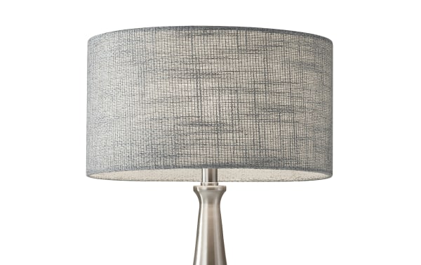 Mid-century modern Lisette Brushed Steel Table Lamp with gray fabric drum shade, brushed steel base, clear cord, and 3-way rotary switch.
