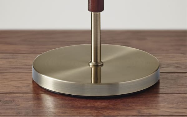 Antique brass circular metal base of Alliston 65.5'' Mid-Century Modern floor lamp with walnut eucalyptus wood accents on taupe hardwood floor.