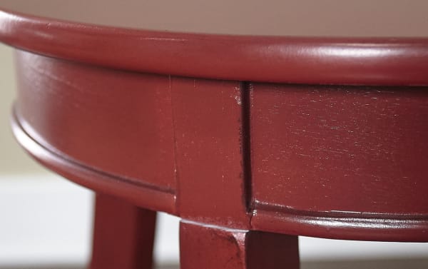 Close-up of Loudain Red Round Table's curved edge and tapered leg, showcasing its smooth red finish and transitional style in MDF and rubberwood.