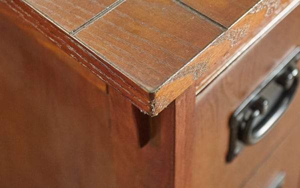 Close-up of Christy Brown Storage Cabinet Side Table corner showing rich brown rubberwood solids with traditional carved edges and dark metal handle pull in transitional style