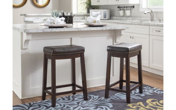 Transitional Cielo brown faux leather backless counter stool with rubberwood frame, antique brass nailhead trim, and double needle stitching on seat.