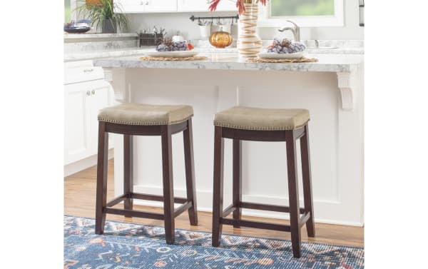 Cielo Beige Faux Leather Backless Counter Height Stool with deep brown rubberwood frame, beige polyurethane seat, antique brass nailhead trim, and transitional style.