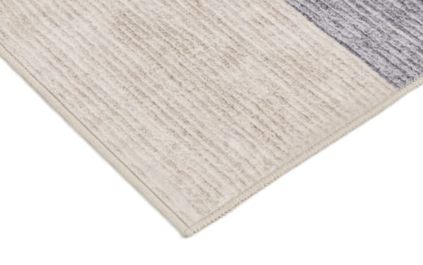 Corner close-up of Kwesi 8' x 10' Purple Oriental washable rug showing beige and blue transitional polyester fabric with textured stripe pattern and stitched edge.