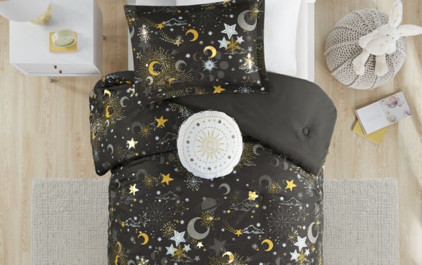 Despia Starry Sky Full/Queen comforter set in charcoal with gold, white, and gray celestial prints. Glam microfiber polyester bedding with reversible design featuring stars, moons, and sun motifs for a cosmic-themed bedroom. Includes matching pillow shams and decorative round pillow with embroidered sun.