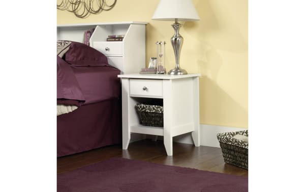 Janis White Nightstand with Drawer in transitional style, made of white wood with smooth metal runner drawer and open bottom shelf for bedside storage.