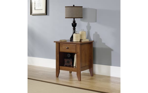 Janis Natural Nightstand with Drawer in warm wood finish, transitional style, featuring smooth metal runner drawer and open bottom shelf for bedside storage.