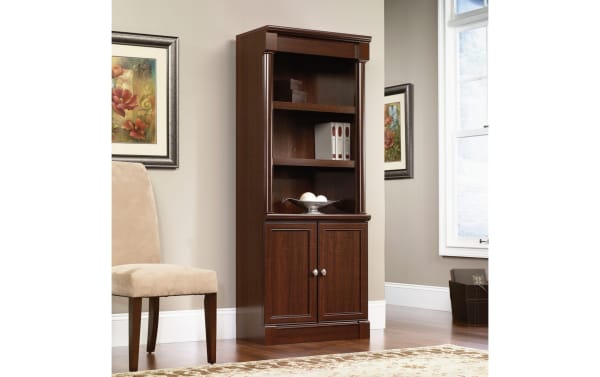 Transitional Detlof 71.9" cherry particle board bookcase with two adjustable shelves, hidden cabinet storage, silver knobs, and slide-on moldings.