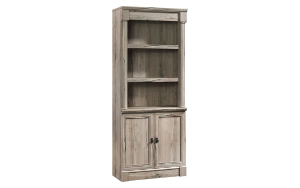 Tall wooden bookcase with two shelves and a two-door cabinet below, featuring a rustic light brown finish and decorative molding.