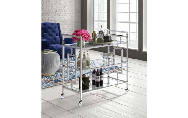 Contemporary Oakley Silver Bar Cart with three tempered glass shelves, chrome frame, geometric side details, and caster wheels for mobility.
