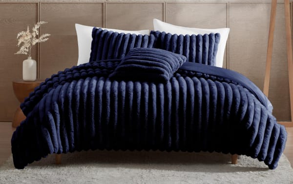 Luxurious navy blue ribbed plush bedding set on a modern wooden bed frame, featuring matching pillows and a soft textured comforter.