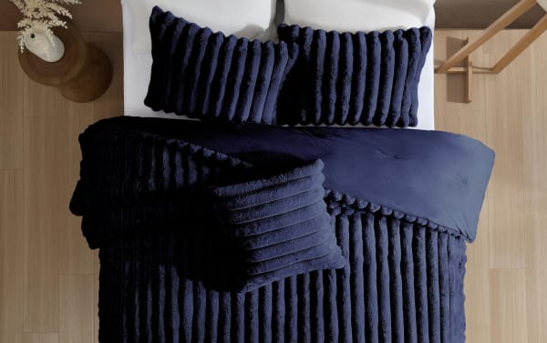 Luxurious navy blue ribbed plush bedding set with matching pillows on a white mattress, styled in a modern bedroom with light wood flooring.
