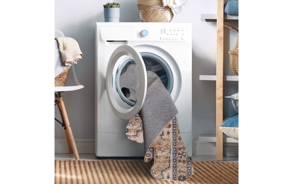 Front-loading washing machine with a beige and ivory Norah 5' x 7' Traditional washable rug made of stain-resistant polyester fabric partially inside.