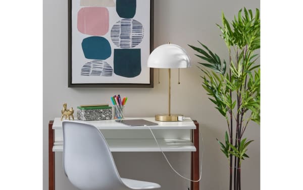 Contemporary Juni table lamp with white metal dome shade and antique brass base, featuring built-in AC outlet for device charging, ideal for mid-century modern décor.