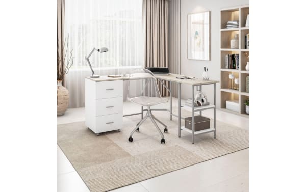 Kyla Natural & White 3 Drawer L-Shaped Desk with MDF top, steel frame, three white drawers, two adjustable shelves, and clear plastic swivel chair in a bright home office.
