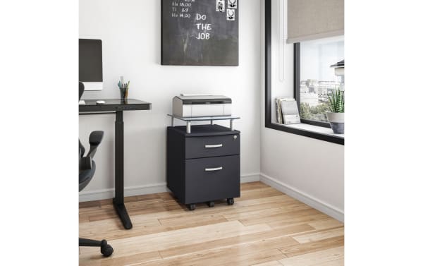 Adrian Graphite 2 Drawer File Cabinet in contemporary style with locking top drawer, hanging file drawer, tempered glass shelf, powder-coated steel supports, and five casters for mobility in a modern office setting.