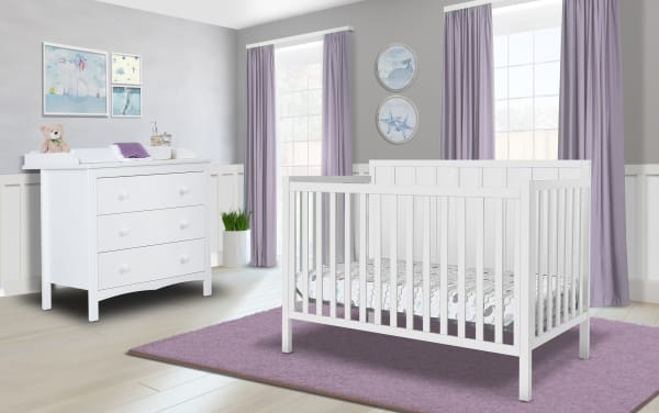 Ollie White 4-in-1 Convertible Crib in transitional farmhouse style, made of white pine solids and laminated veneer lumber, with sleek modern lines, shown in nursery with matching white dresser and lavender curtains.