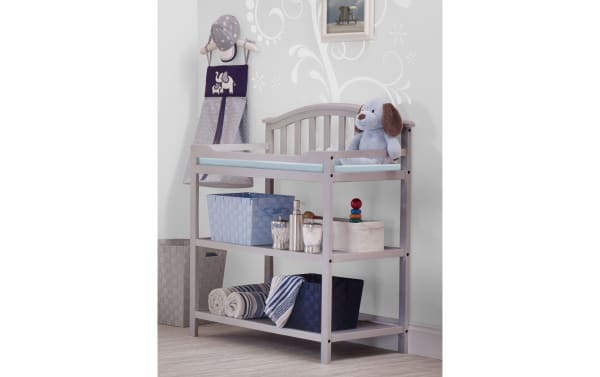 Finlay Gray transitional changing table in gray pine solids with curved back silhouette, safety belt, padded top, and two storage shelves.