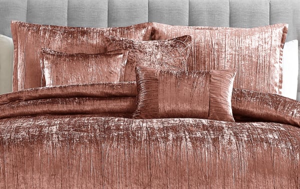 Luxurious crushed velvet bedding set in rich copper color, featuring a comforter, multiple decorative pillows, and shams with a soft, textured finish.