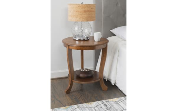 Madison 22'' brown round side table in contemporary style, made of solid acacia, MDF, and paper veneer, with curved apron, three tapered legs, lower shelf, and smooth tabletop for display or storage.