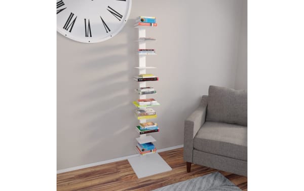 Contemporary Darin White Tower Shelf made of powder-coated iron, featuring stacked flat shelves for books or decor, styled as a white sculptural storage unit next to a gray sofa on wooden flooring.