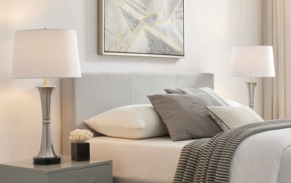 Contemporary Ferrara brushed nickel table lamps set of 2 with white fabric shades, metal candlestick bases, and built-in USB ports on gray nightstands.