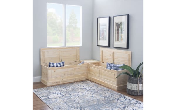 Corner storage bench set made of light natural wood with hinged lids, featuring blue and white checkered cushions, placed in a modern room with framed wall art and a patterned blue rug.