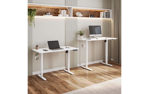 Two adjustable white standing desks of different heights in a modern home office with wood flooring, wall shelves, and LED lighting.