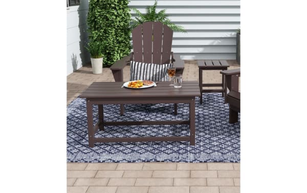 Paloma Dark Brown Outdoor Adirondack Coffee Table in contemporary style, made of durable high-density plastic, shown on a patterned outdoor rug with matching Adirondack chairs.