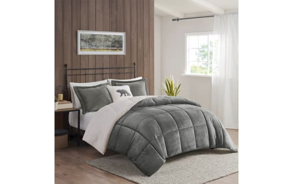 Gray velvet plush comforter set with sherpa lining on a bed with matching gray pillows and a decorative bear pillow in a bright bedroom.