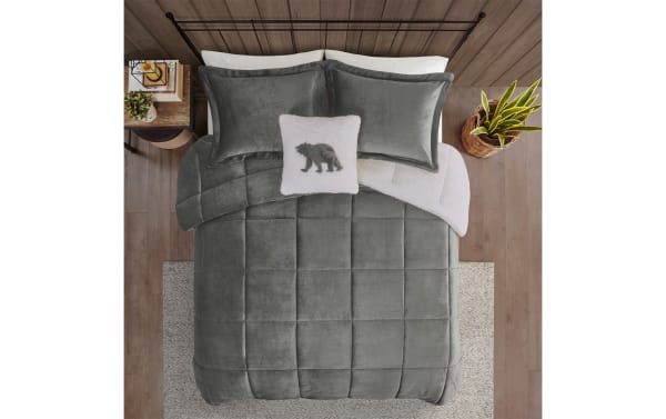 Gray velvet comforter set with two matching pillows and a white decorative pillow featuring a gray bear design on a wooden floor background.