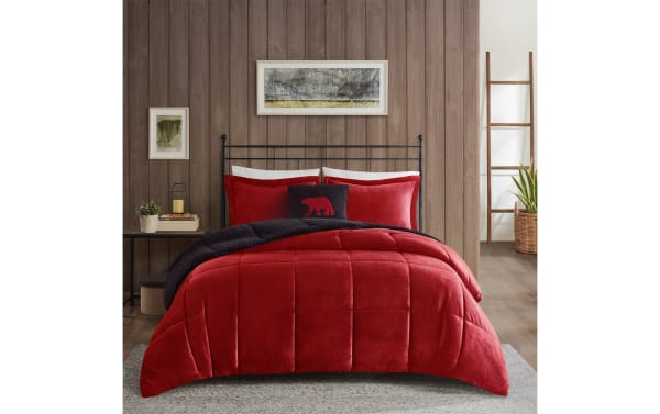 Red velvet comforter set with black sherpa lining on metal bed frame, featuring matching red pillows and decorative bear pillow in cozy bedroom setting.