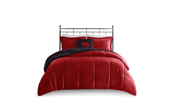 Red and black velvet comforter set on a black metal bed frame, featuring plush pillows and a decorative bear-themed throw pillow.